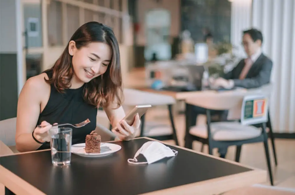 Customer using phone while eating cake at table in restaurant