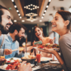 Group of happy people sitting at a restaurant table, smiling and laughing while enjoying their meal. The table is filled with delicious food and drinks, creating a warm and joyful atmosphere